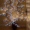 A decorative branch light featuring blue LED cherry blossoms displayed in a dark vase.