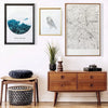 A gallery wall featuring framed artwork, including a blue landscape print and a black and white line drawing, displayed on a 