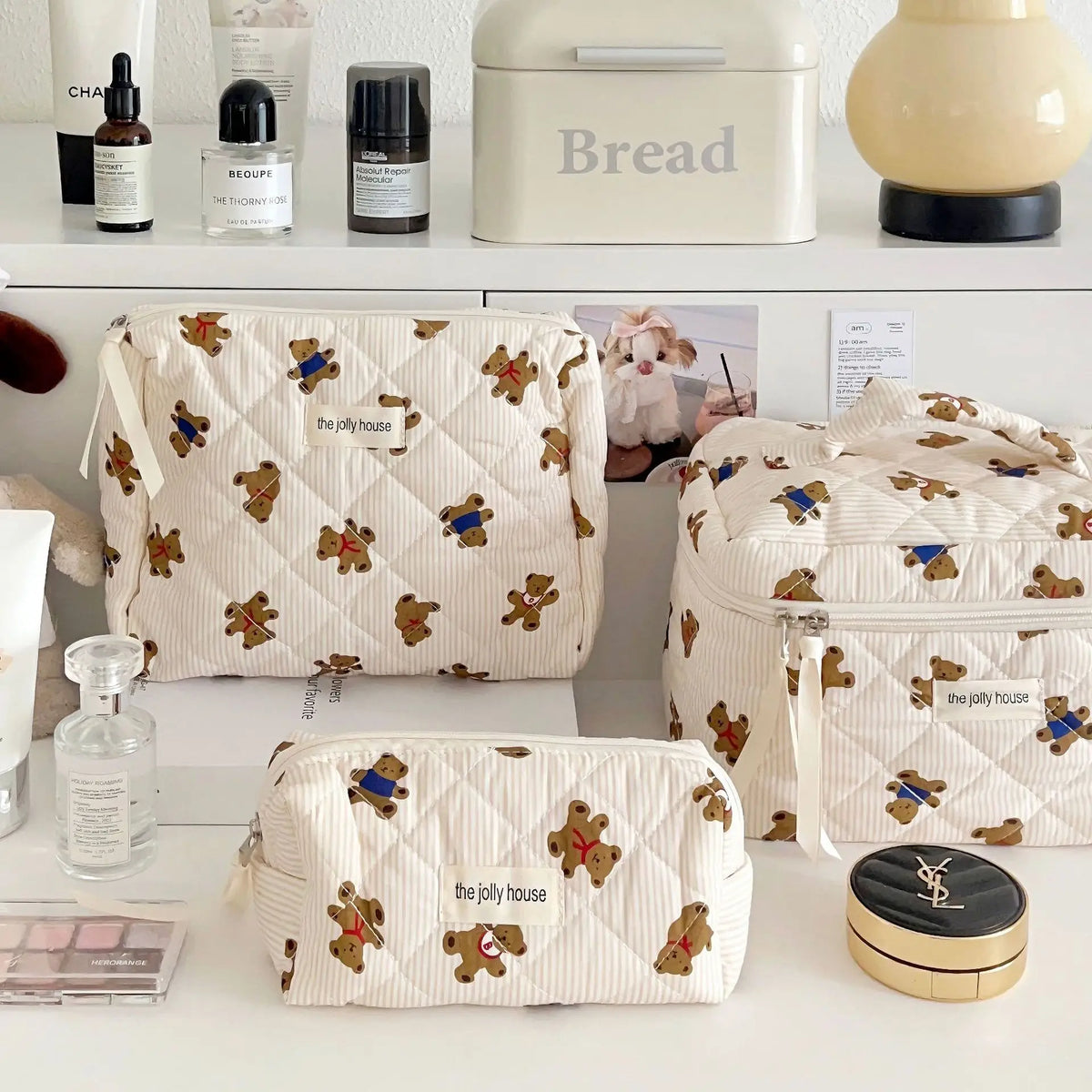 Eine Sammlung von beige- und weiß bear-förmigen Make-up-Taschen und einer cremefarbenen Brotkasten auf einer weißen Oberfläch