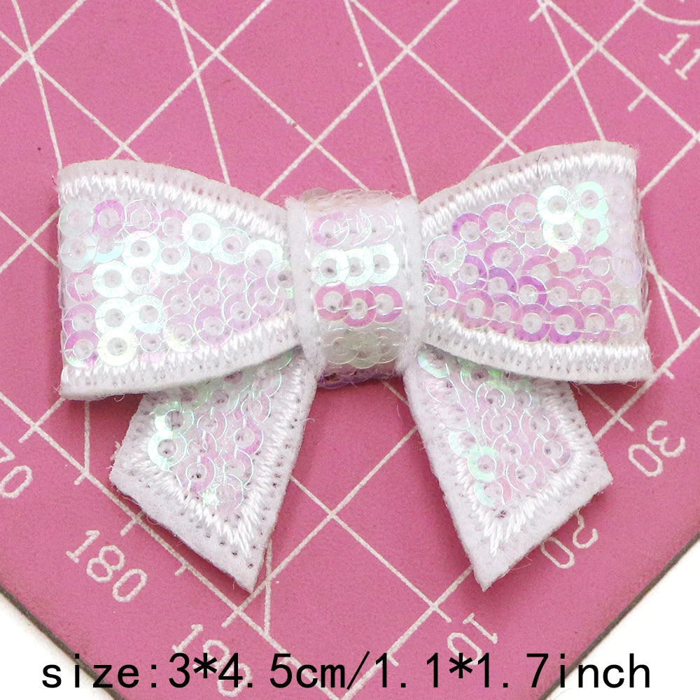 A set of five white and pink sequin bow patches for DIY crafts displayed on a pink grid background.