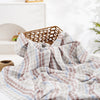 A soft, plaid muslin baby swaddle blanket draped over a woven basket in a bright, airy setting.