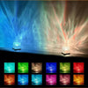 An 16-color ocean wave aurora projector night light displays vibrant blue and pink light beams against a dark background.