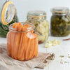 A glass jar filled with bright orange carrots resting on a linen cloth.