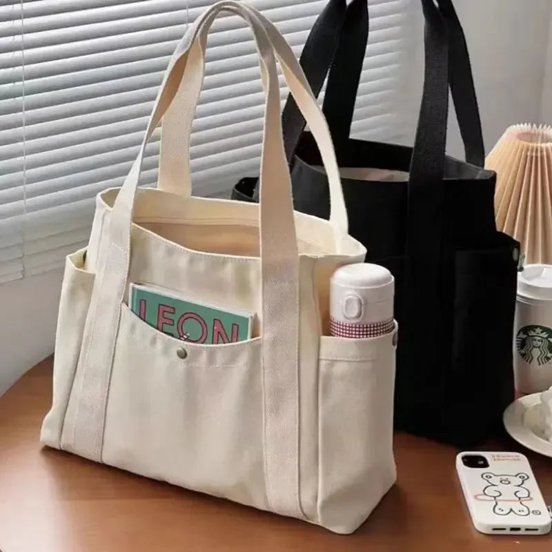 Una bolsa de tela beige con un bolsillo que contiene un objeto cilíndrico blanco y un smartphone pequeño.