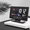 A black digital weather station clock displaying time, temperature, and humidity on a white stand.