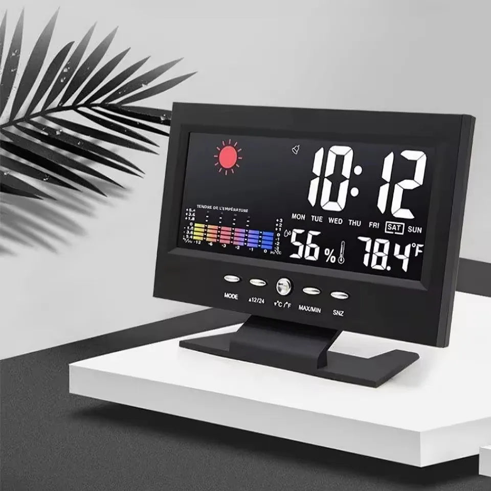 A black digital weather station clock displaying time, temperature, and humidity on a white stand.