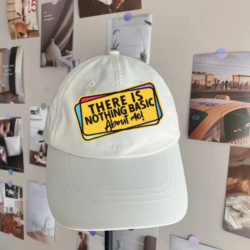 A white baseball cap with a yellow embroidered patch that reads There Is Nothing Basic About Me