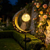 A solar moon-shaped garden light featuring an owl and a glowing glass ball mounted on a stone wall.