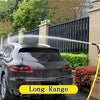 A black car is being washed by a high-pressure water jet from a gun against a dark fence.