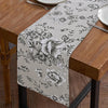 A beige floral patterned table runner displayed on a wooden table.