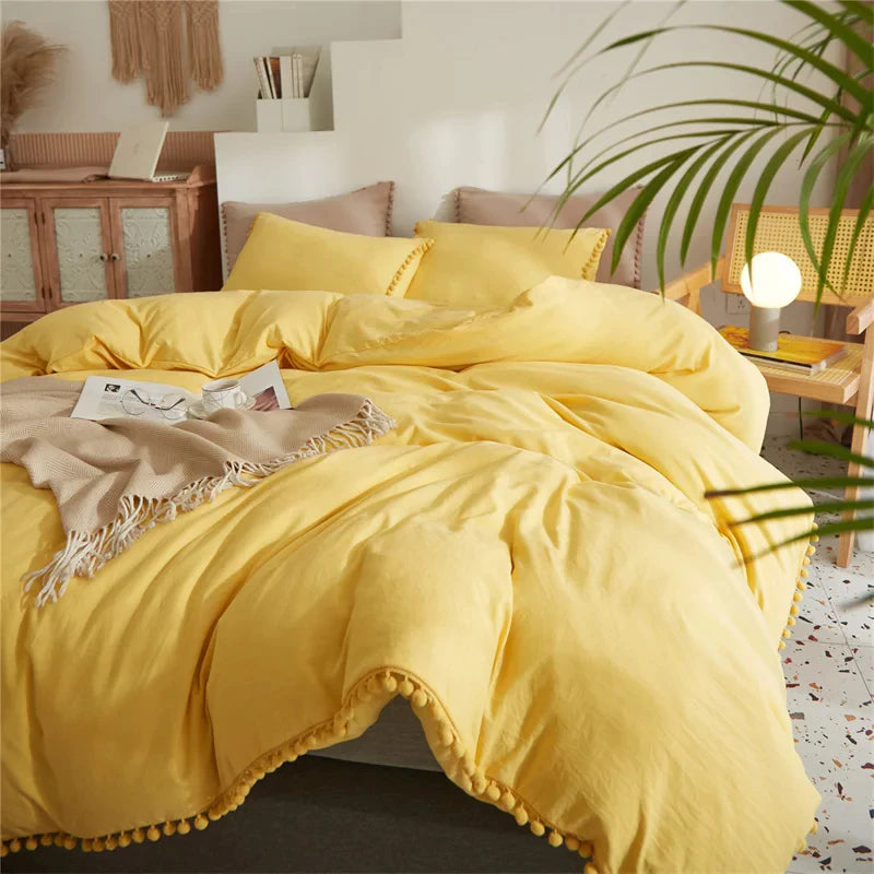 A bright yellow duvet cover set with pom tassels and a beige throw draped over a bed.