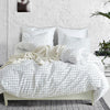 A white and gray plaid duvet cover set with pillows and a cream knit throw on a bed.