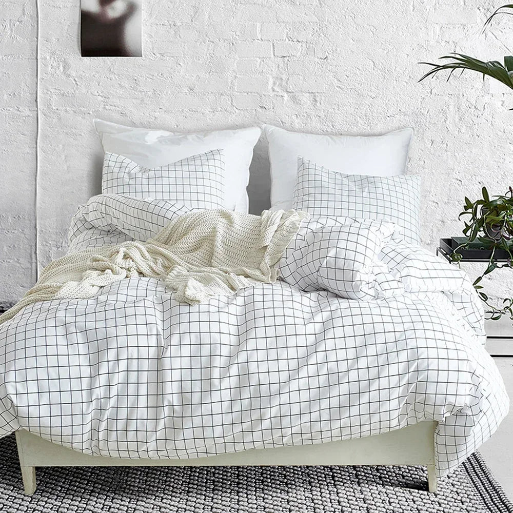 A white and gray plaid duvet cover set with pillows and a cream knit throw on a bed.