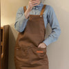 A person wearing a brown leather apron over a light blue shirt, holding a phone.