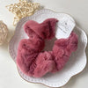 A fluffy, dusty rose colored plush coil hair tie is displayed on a white plate.