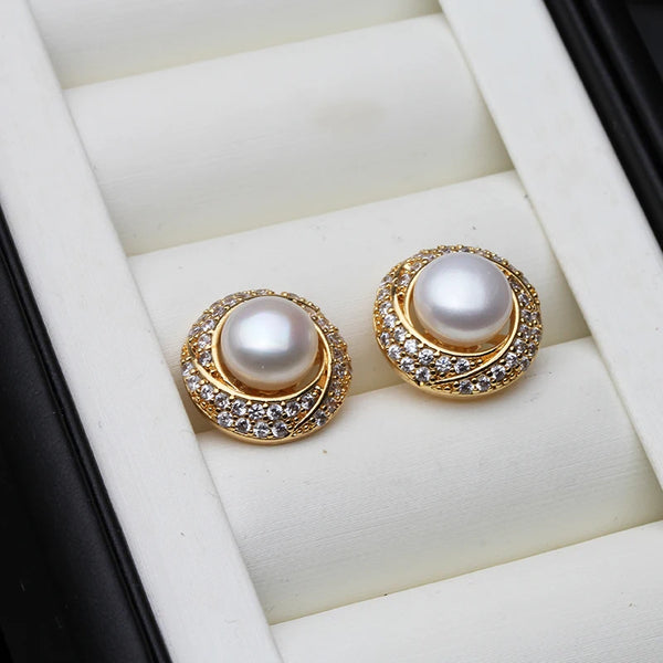 Boucles d'oreilles à clous dorés avec une perle d'eau blanche entourée de petites pierres claires.