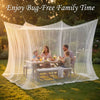 A family enjoying time under a large sheer white mesh fly net canopy on a grassy lawn.