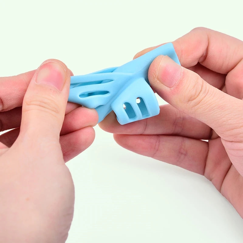 A hand holds a light blue ergonomic pencil grip trainer for posture correction.