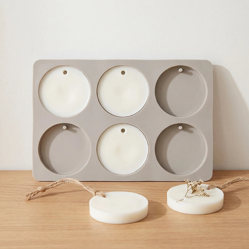 A gray silicone mold with six circular cavities is shown alongside two white soap discs.