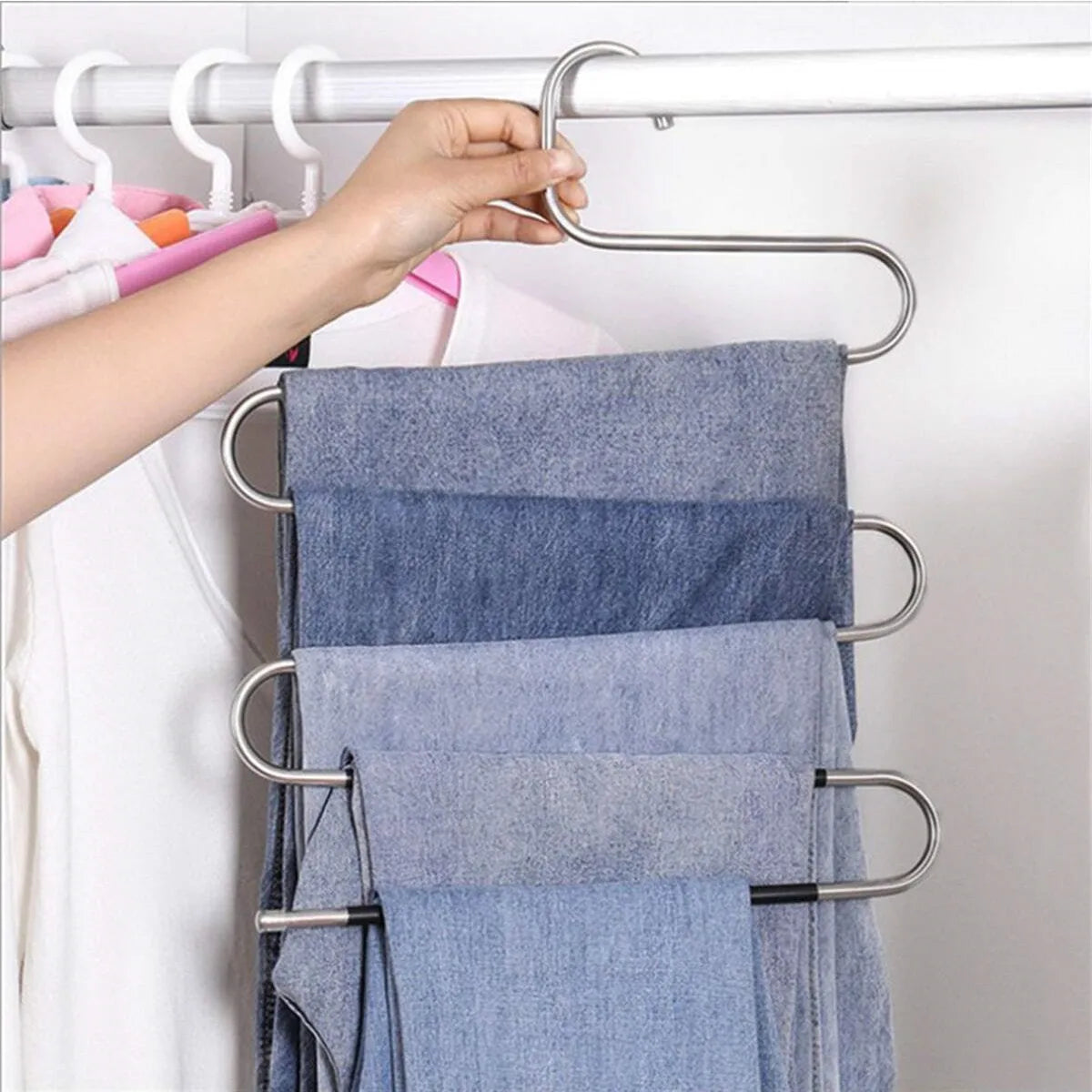 A hand is hanging a folded blue denim towel onto a metal S-shaped pants hanger rack.