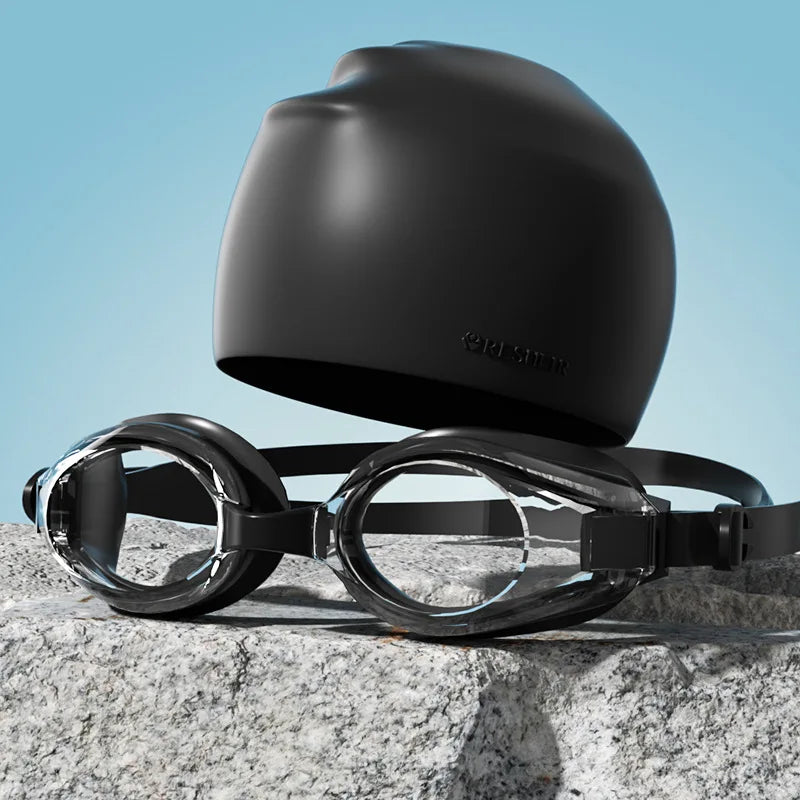 Gafas de natación negras HD antiempañantes con sello de silicona sobre una roca gris.