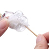 A white fluffy keepsake fur storage pendant keychain is being held by a hand and attached to a wooden stick.