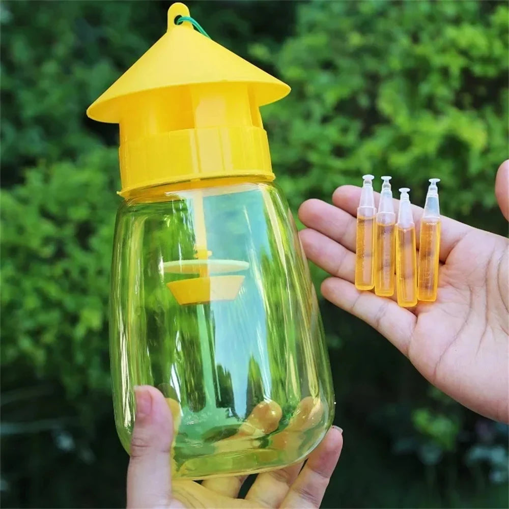 A hand holds a yellow fruit fly trap kit with a glass jar and several small vials of pheromone lure in an outdoor setting.