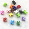 A collection of ten mixed alphabet letter beads in various colors including green, orange, purple, and pink, scattered on a w
