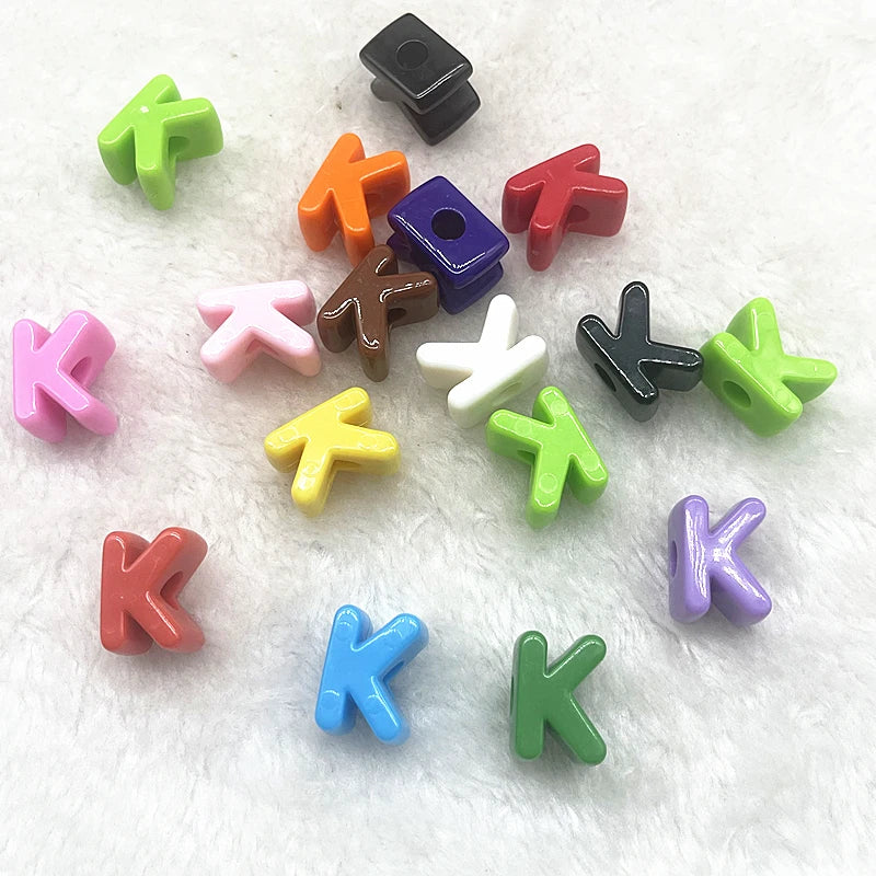 A collection of ten mixed alphabet letter beads in various colors including green, orange, purple, and pink, scattered on a w