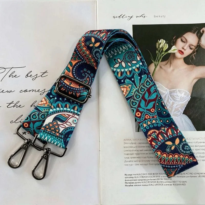 A close-up of an elegant floral patterned fabric strap for a bag, featuring teal and navy blue colors.