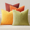 A collection of nine textured corduroy throw pillows in shades of orange, terracotta, and lime green.