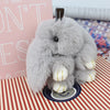A fluffy gray bunny keychain with a pom pom tail resting on a patterned surface.