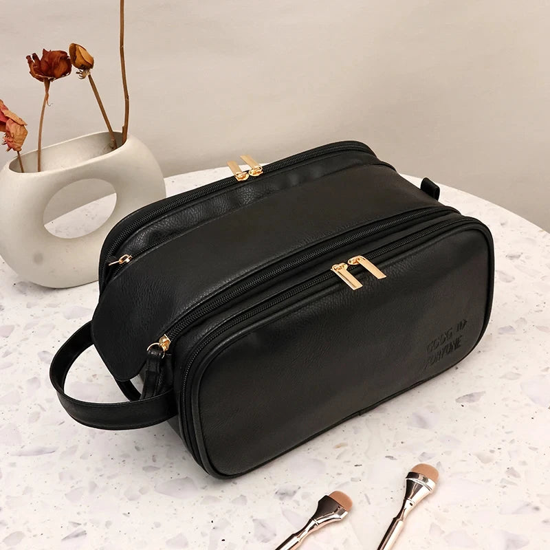 A black waterproof PU leather cosmetic bag lying on a white surface next to dried rose petals and a gold-toned brush.