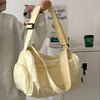 A beige canvas travel tote bag with a light tan crossbody strap being held by a person.