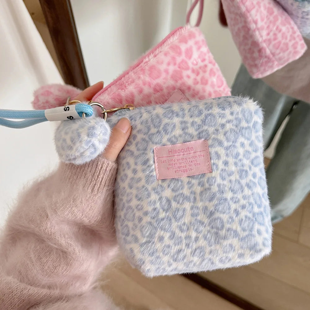 A hand holds a light blue leopard print cosmetic bag with pink and white fuzzy trim.