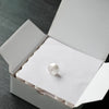 A white embroidery bobbin is placed inside a cardboard box for home embroidery machines.