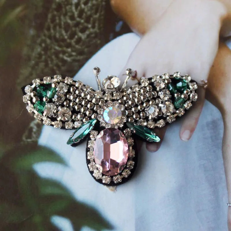 A handcrafted rhinestone bee sew-on patch is held in a person's hand against a light fabric background.