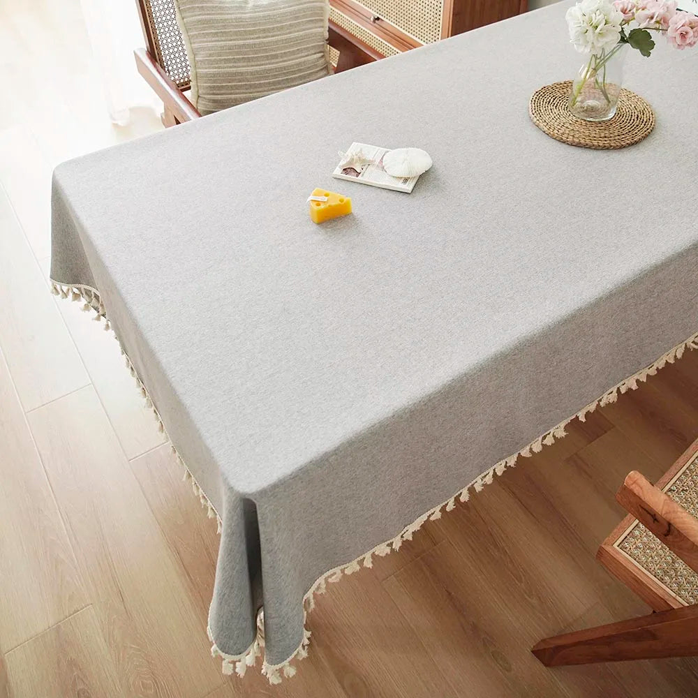 A gray farmhouse tablecloth with white cotton tassels is laid on a wooden dining table.
