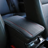 Black leather car armrest cover with a textured storage pad and red stitching.
