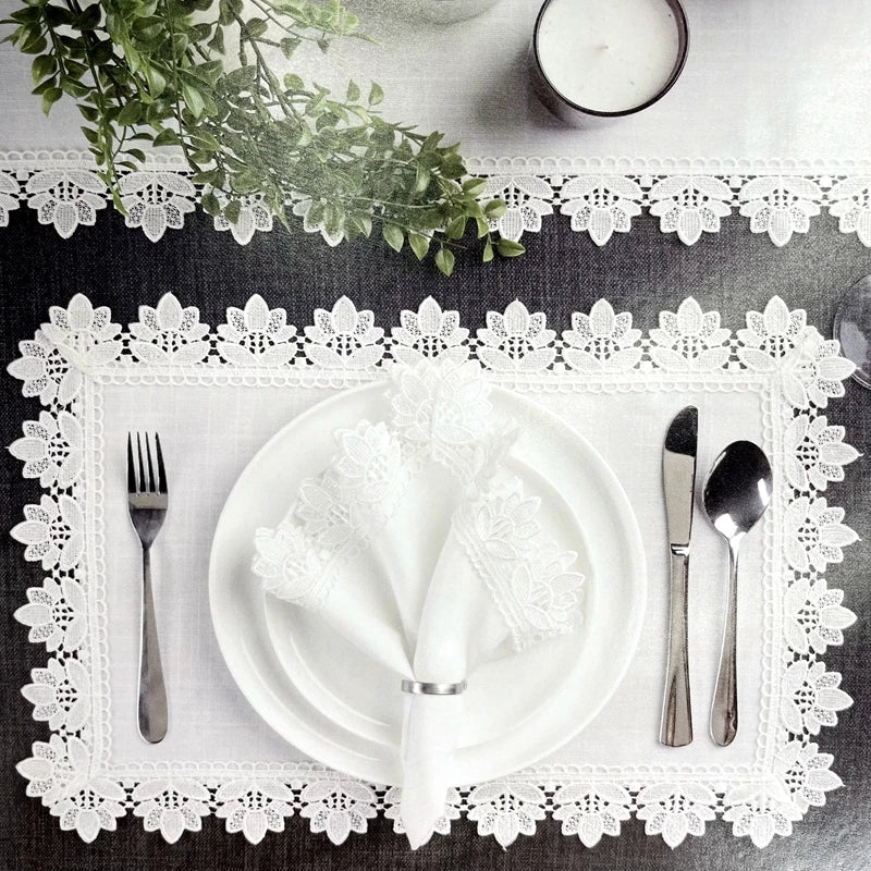 A white dinner plate set with linen hemstitch napkins and silverware displayed on a lace doily.