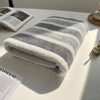 A folded striped bath towel with white and gray stripes resting on a white surface.