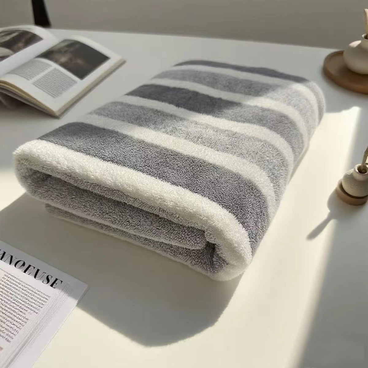 A folded striped bath towel with white and gray stripes resting on a white surface.
