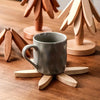 A set of wooden tree-shaped heat-resistant trivets and a ceramic mug resting on a wooden surface.