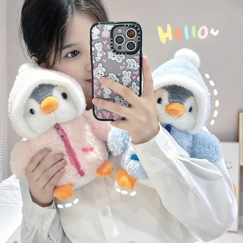 A person holds a pink penguin plush toy with a blue hat and a white penguin plush toy, posing for a photo.