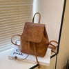 Petit sac à dos de mini en cuir marron avec cordon, exposé sur une surface blanche près d'un store.