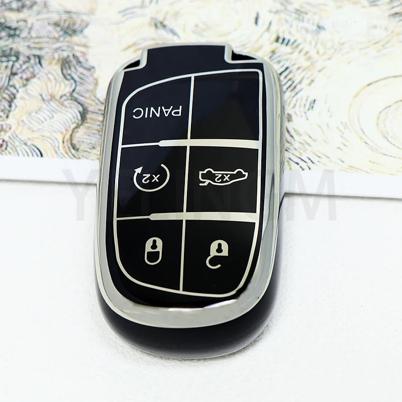 A black TPU car key fob cover with panic and lock buttons is shown against a light patterned background.
