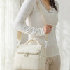 A woman wearing a white long-sleeved top holds a cream insulated lunch bag.