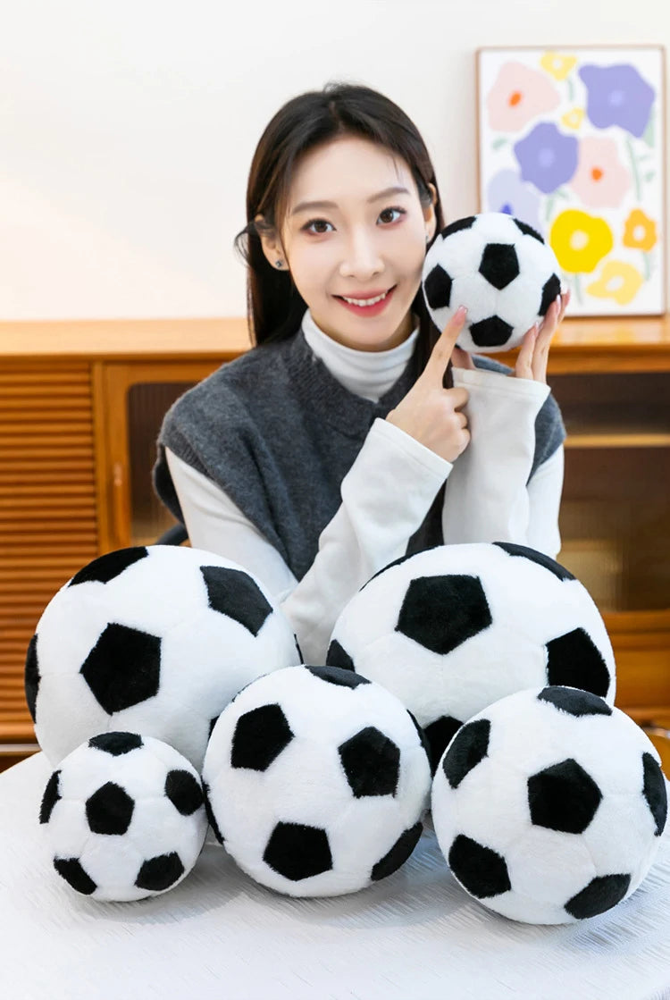 A woman holds a black and white football plush pillow against her chest.