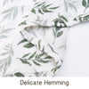 Close-up of a white muslin baby swaddle blanket with green leaf print, showing delicate hemming.