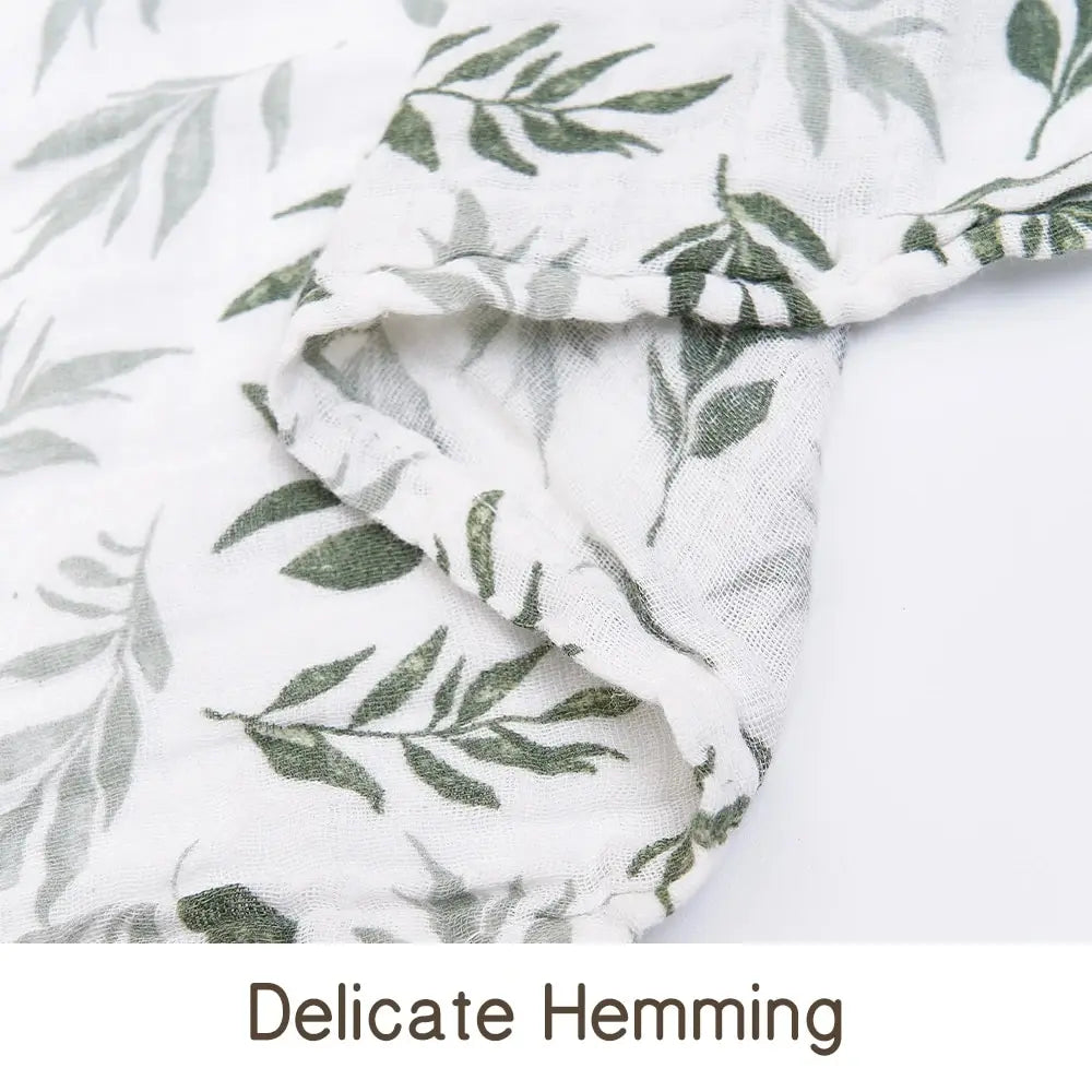 Close-up of a white muslin baby swaddle blanket with green leaf print, showing delicate hemming.